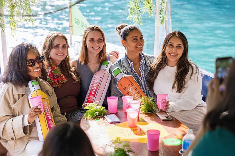 Five women on a boat holding bottle plushies
