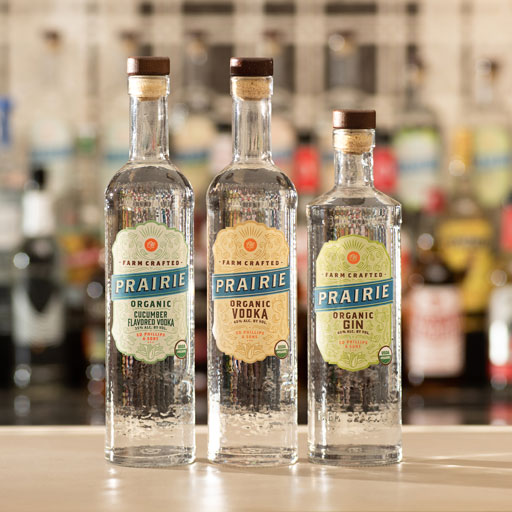 The two bottles of Prairie Organic vodka and one bottle of gin on a bar